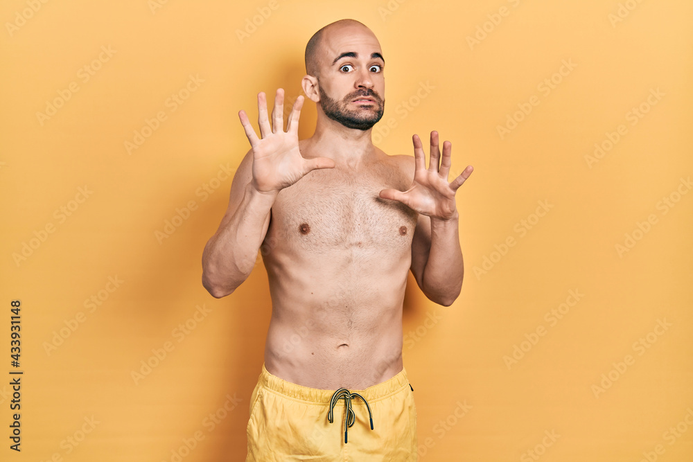Fototapeta premium Young bald man wearing swimwear afraid and terrified with fear expression stop gesture with hands, shouting in shock. panic concept.