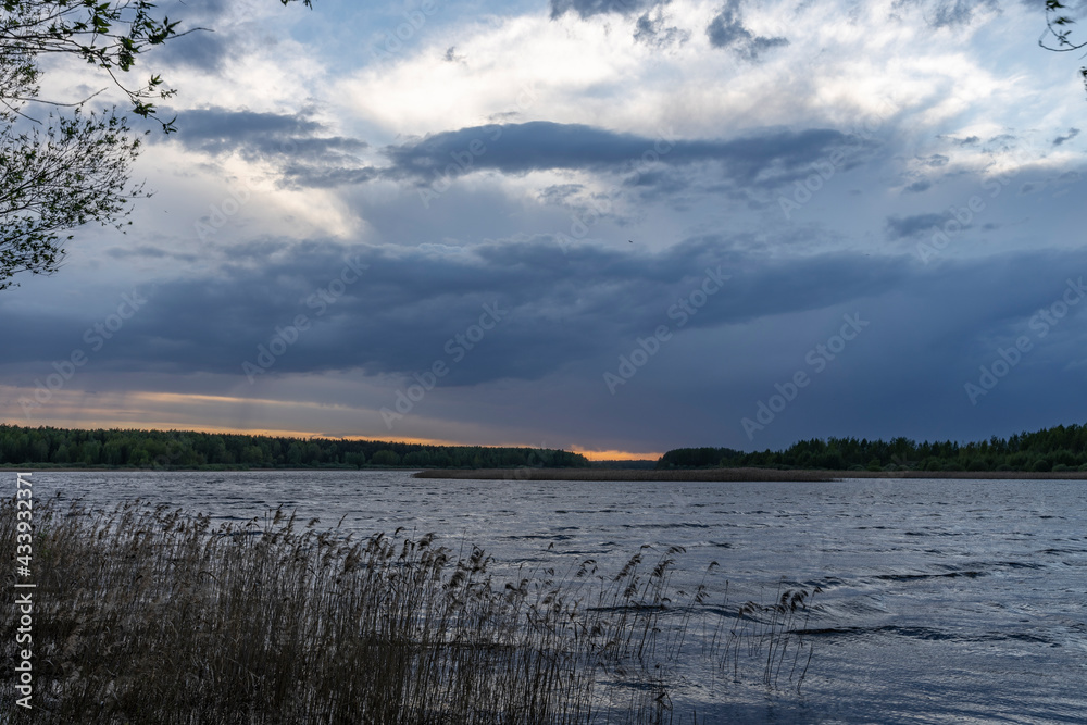 Obraz premium Evening landscape with a river and clouds. Dramatic sunset over the river. Dry grass in the river.