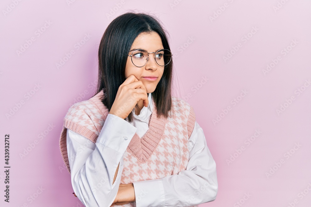 Young brunette woman wearing elegant sweater and glasses serious face thinking about question with hand on chin, thoughtful about confusing idea Young brunette woman wearing elegant sweater and glasses serious face thinking about question with hand on chin, thoughtful about confusing idea