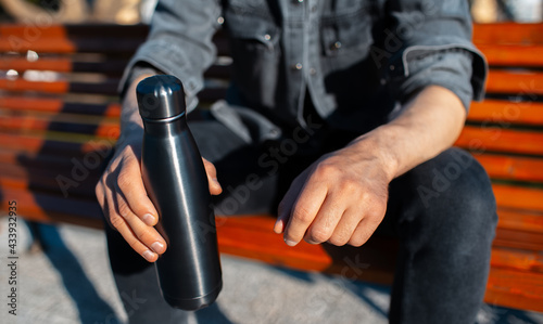 Close-up of male hands  holding steel reusable thermo water bottle of black.