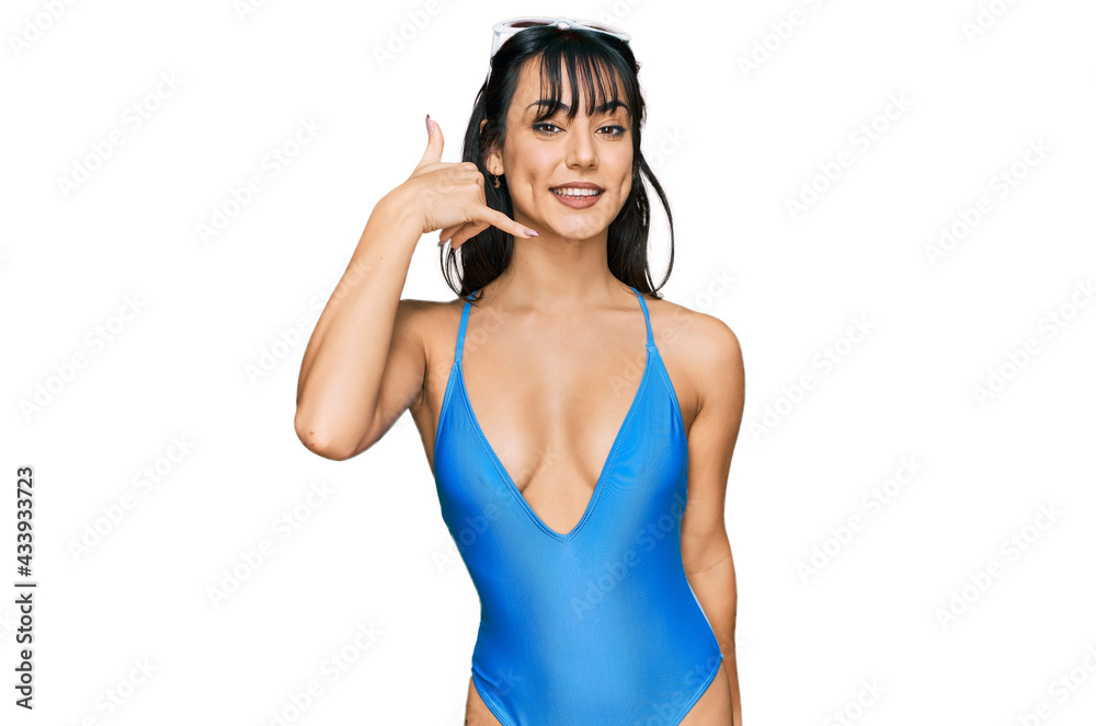 Young hispanic woman wearing swimsuit and sunglasses smiling doing phone gesture with hand and fingers like talking on the telephone. communicating concepts. Young hispanic woman wearing swimsuit and sunglasses smiling doing phone gesture with hand and fingers like talking on the telephone. communicating concepts.