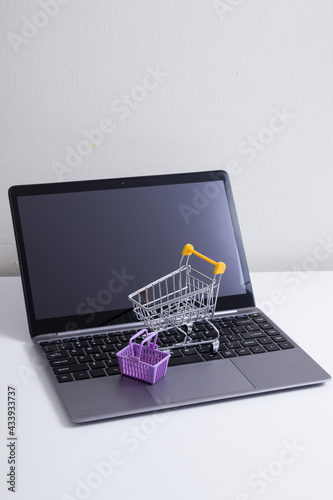 Open laptop with supermarket trolley and basket on the table. Online shopping from home
