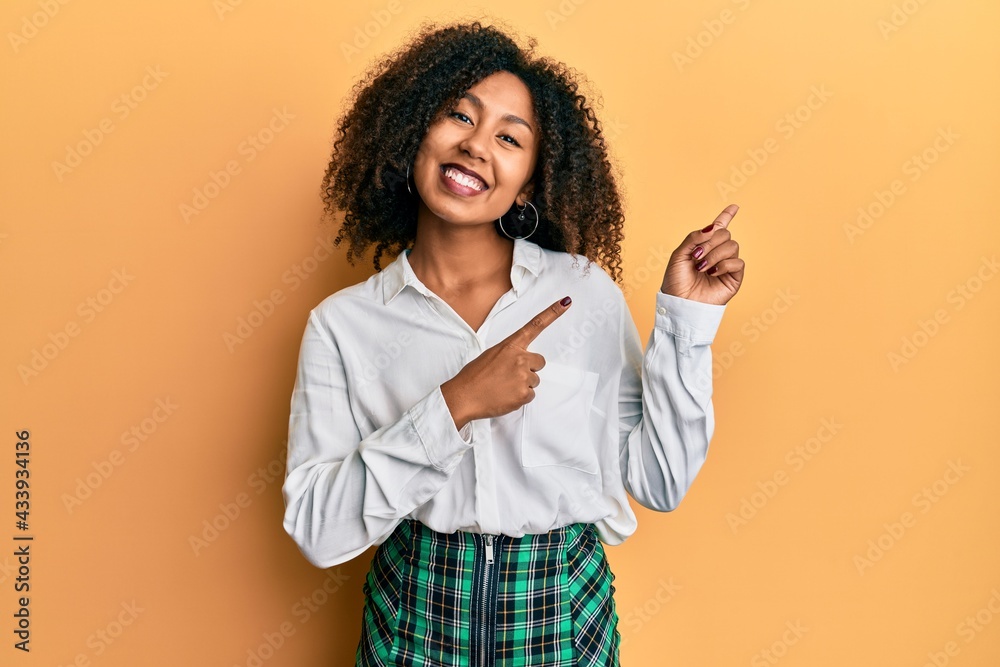 Beautiful african american woman with afro hair wearing scholar skirt smiling and looking at the camera pointing with two hands and fingers to the side. Beautiful african american woman with afro hair wearing scholar skirt smiling and looking at the camera pointing with two hands and fingers to the side.