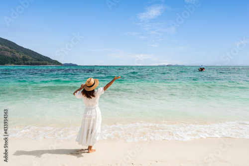 Young woman traveler relaxing and enjoying at beautiful tropical white sand beach with wave foam and transparent sea, Summer vacation and Travel concept