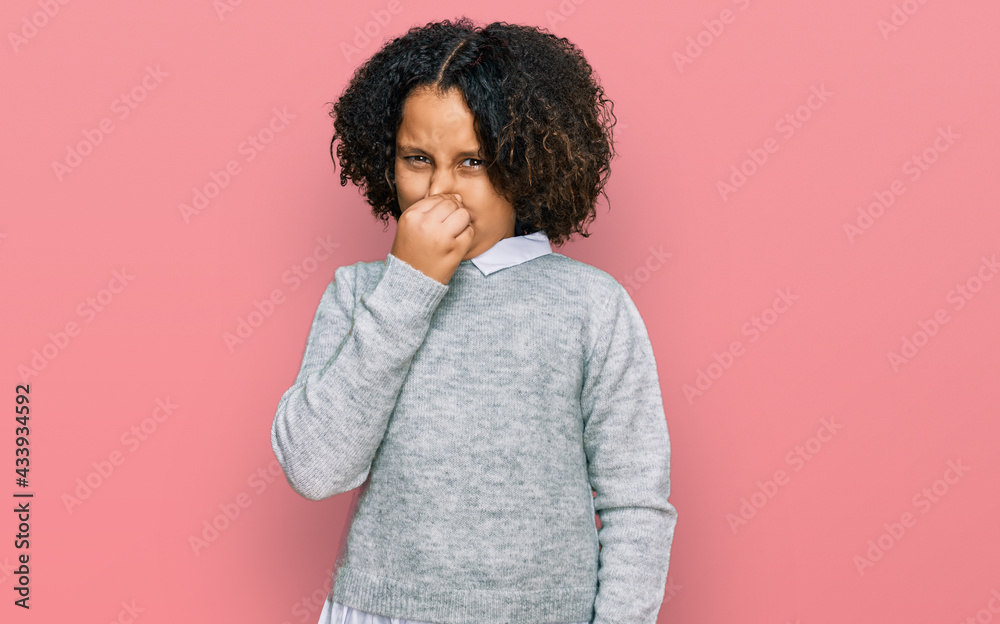 Young little girl with afro hair wearing casual clothes smelling something stinky and disgusting, intolerable smell, holding breath with fingers on nose. bad smell Young little girl with afro hair wearing casual clothes smelling something stinky and disgusting, intolerable smell, holding breath with fingers on nose. bad smell