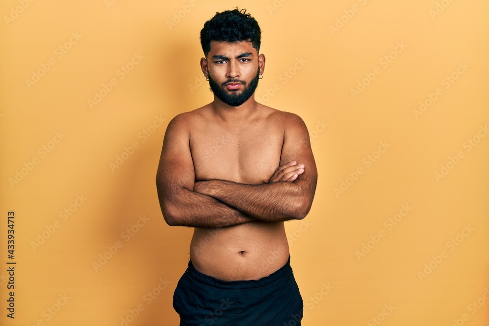 Arab man with beard wearing swimwear shirtless skeptic and nervous, disapproving expression on face with crossed arms. negative person.