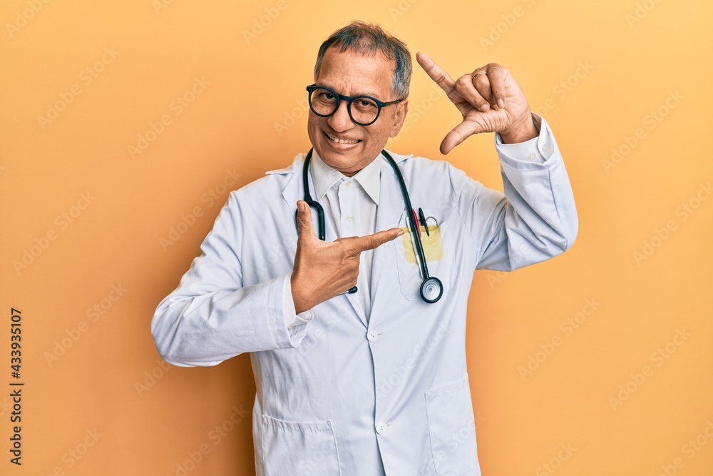 Middle age indian man wearing doctor coat and stethoscope smiling making frame with hands and fingers with happy face. creativity and photography concept. Middle age indian man wearing doctor coat and stethoscope smiling making frame with hands and fingers with happy face. creativity and photography concept.