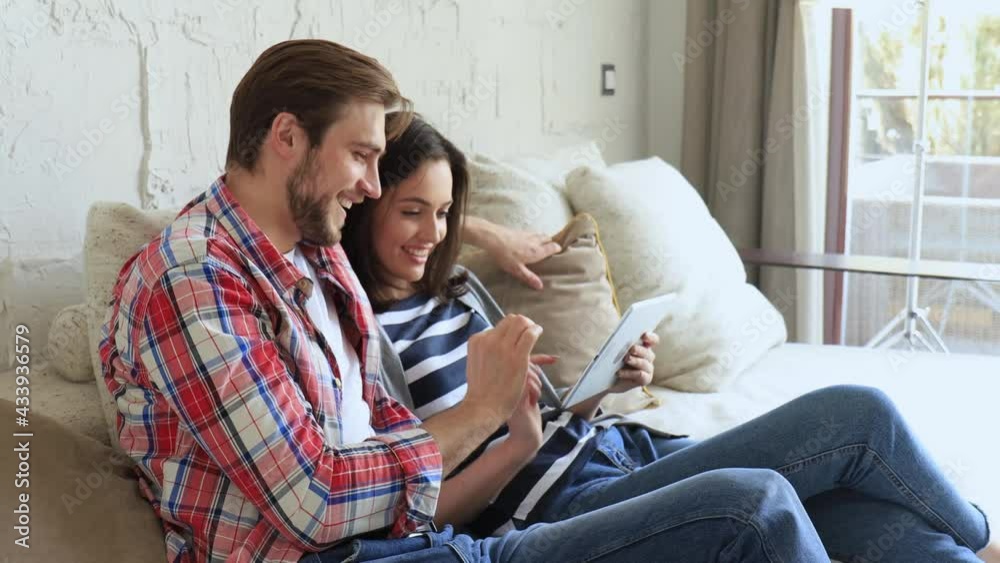 Young couple watching media content online in a tablet sitting on a sofa in the living room