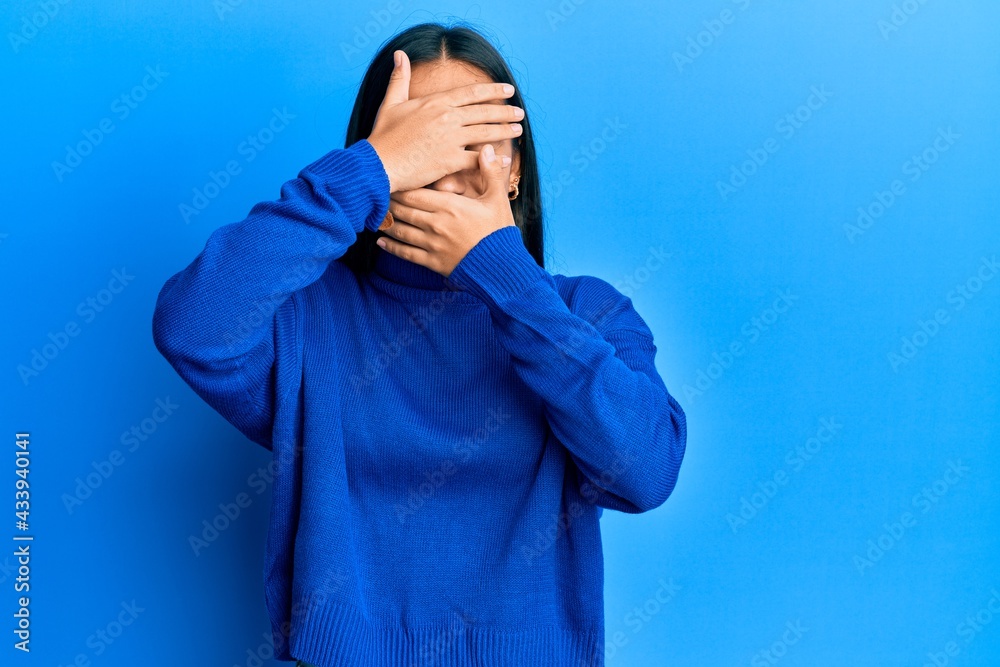 Young asian woman wearing casual winter sweater covering eyes and mouth with hands, surprised and shocked. hiding emotion Young asian woman wearing casual winter sweater covering eyes and mouth with hands, surprised and shocked. hiding emotion
