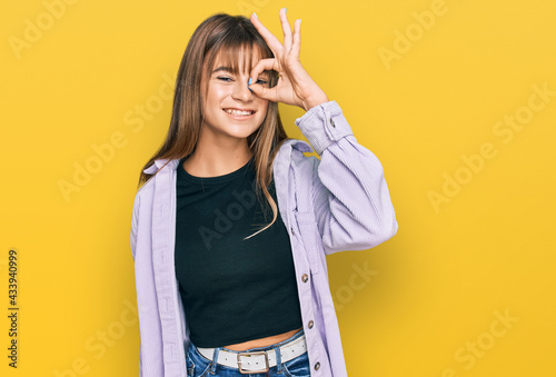 Teenager caucasian girl wearing casual clothes doing ok gesture with hand smiling, eye looking through fingers with happy face.