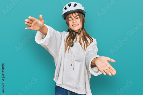 Teenager caucasian girl wearing bike helmet looking at the camera smiling with open arms for hug. cheerful expression embracing happiness.