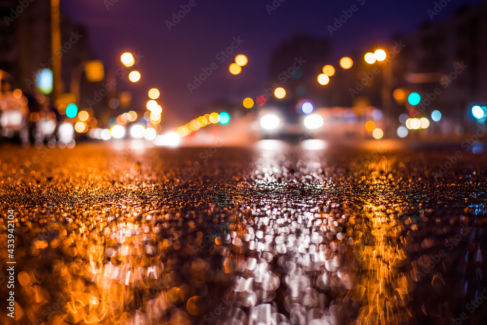 Rainy night in the big city, the car headlights shine through the mist. Close up view from the asphalt level