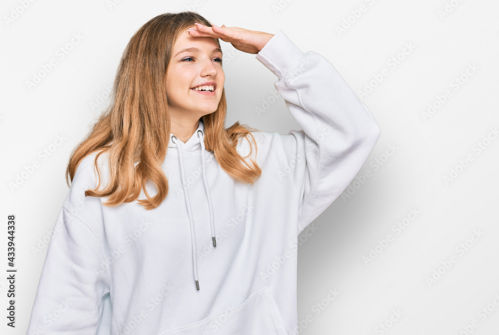 Beautiful young caucasian girl wearing casual sweatshirt very happy and smiling looking far away with hand over head. searching concept. Beautiful young caucasian girl wearing casual sweatshirt very happy and smiling looking far away with hand over head. searching concept.