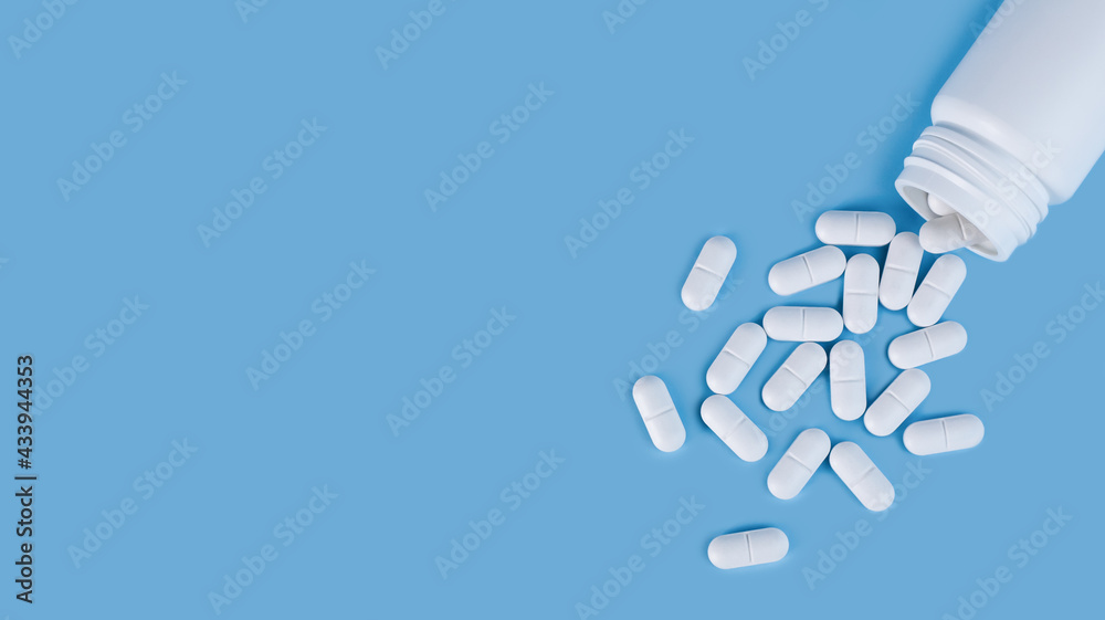 Scattered white pills from the white bottle on blue background. Health care and medicine concept. Close-up. Place for text.