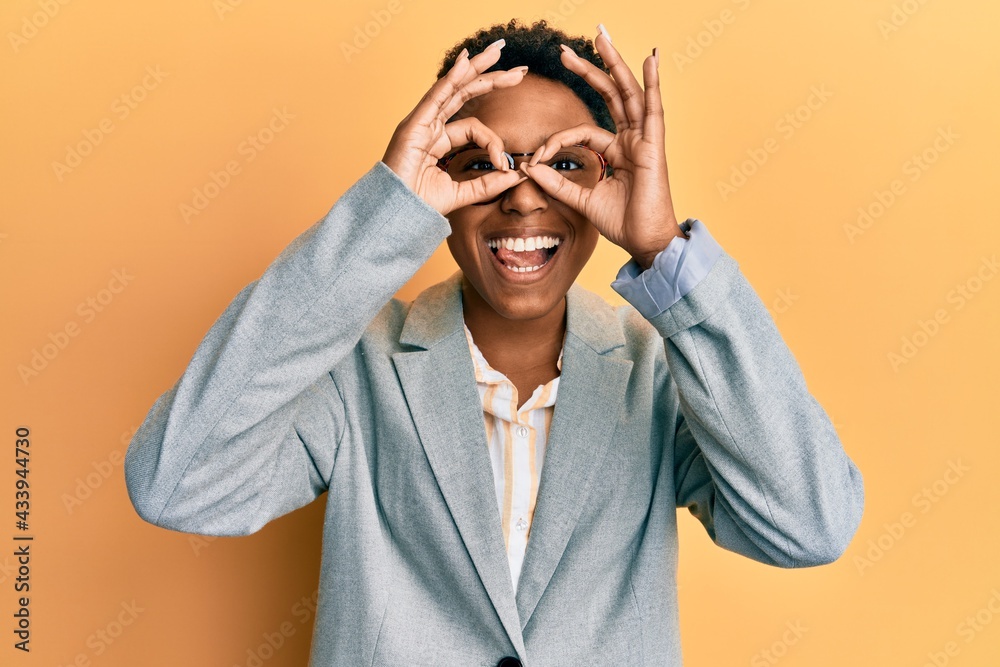 Young african american girl wearing business jacket and glasses doing ok gesture like binoculars sticking tongue out, eyes looking through fingers. crazy expression. Young african american girl wearing business jacket and glasses doing ok gesture like binoculars sticking tongue out, eyes looking through fingers. crazy expression.