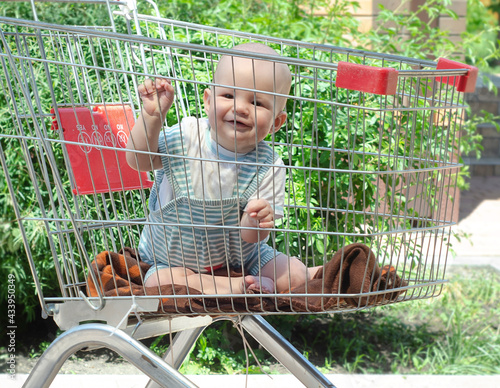 A small child sits in an empty grocery cart from a supermarket.