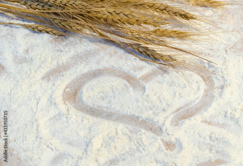 Heart of flour on wooden desk painted by a thinger and wheat ears. valentine concept