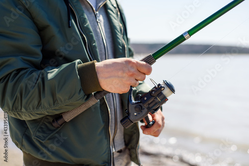A man with a fishing rod is fishing. Close-up of a fishing rod with a reel in the hands of a fisherman. Calm male relaxation