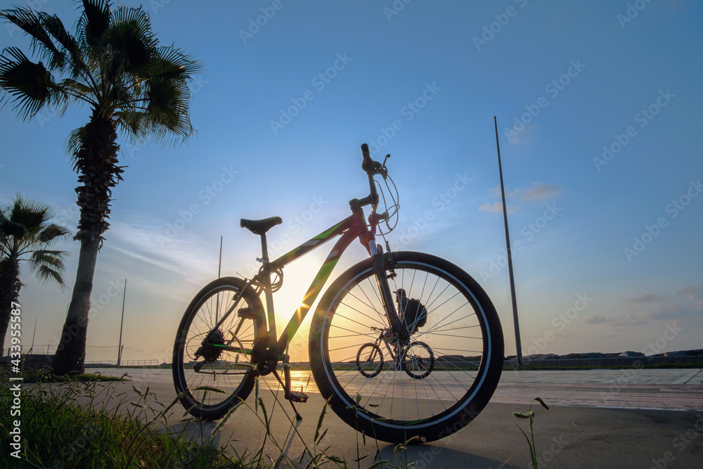 Silhouette of a bike at sunset. The sun shines through the bicycle frame with silhouette of bicycle rider at sea side park