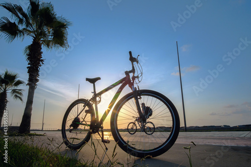 Fototapeta Naklejka Na Ścianę i Meble -  Silhouette of a bike at sunset. The sun shines through the bicycle frame with silhouette of bicycle rider at sea side park