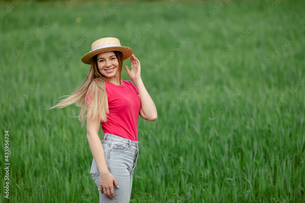 Carefree happy woman in pink t-shirt and straw hat enjoying nature on a meadow of grass.