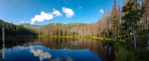 A panoramic view on Smreczynski Staw in Tatra Mountains in Poland. Glacial tarn at the mouth of Pysznianska Valley. The high Tatra chains are reflecting in the calm surface of the lake. White clouds
