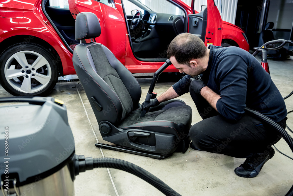 Car service worker cleaning car seat with vacuum cleaner.