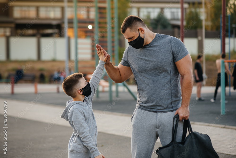 A father and child stand on a sports field in masks after training during sunset