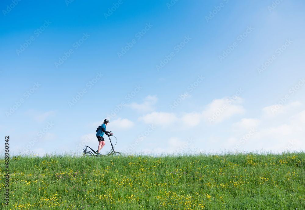 woman rides elliptigo bike on grassy dike in holland under blue sky