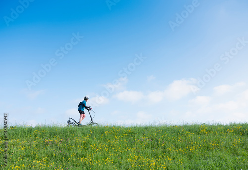 woman rides elliptigo bike on grassy dike in holland under blue sky
