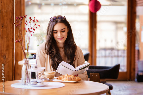 Canvas Attractive young woman sitting in the cafe and reading a book