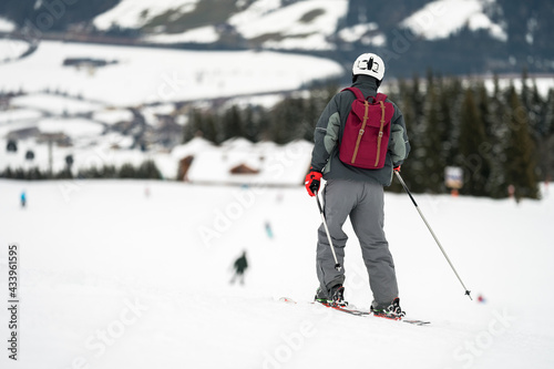 Unidentified tourist skiing in Flachau, the ski resort in Austria. Man in grey sportswear and with red bag. People on bokeh background. View from behind.