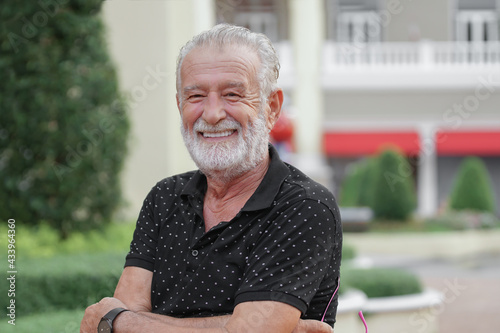 Portrait of happy Caucasian senior kind man with winkles and white beard mustache hairs. Old man is smiling at amusement park