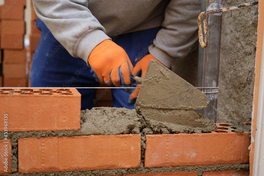 Construction worker putting cement on the brick wall. Man bricklaying