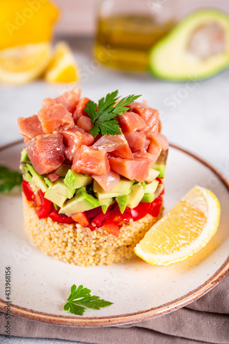 Salmon tartare with tomatoes, avocado and quinoa on a plate and light gray background close up, vertical photo