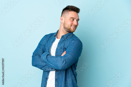 Russian handsome man isolated on blue background with arms crossed and happy