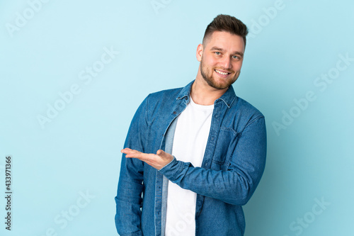 Russian handsome man isolated on blue background presenting an idea while looking smiling towards