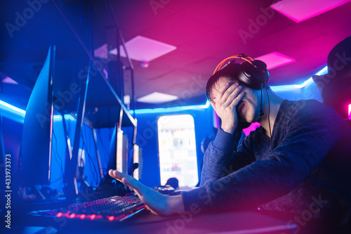 Streamer young man facepalm professional gamer playing online games computer with headphones, neon color photo