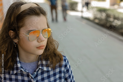 Portrait of a teenage girl in sunglasses aviator looks to the side with apprehension and anxiety on the street, people are passing by.  The concept of waiting for important and serious news.