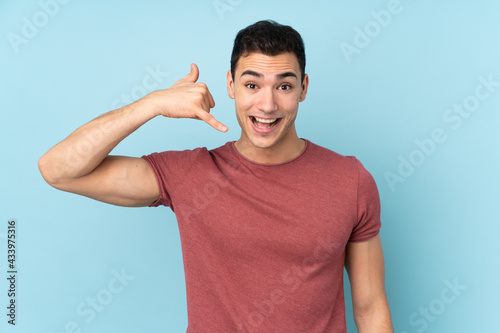 Young caucasian handsome man isolated on blue background making phone gesture. Call me back sign