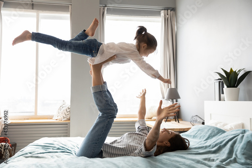 Smiling young mom play have fun with small daughter in home bedroom on family weekend. Happy Caucasian mother and little girl child engaged in funny game activity together. Parenthood concept.