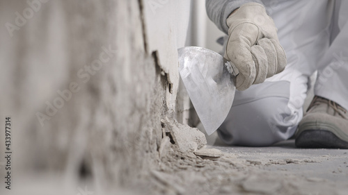 Fotografia Construction worker hands with gloves working with spatula scrape off the plaste