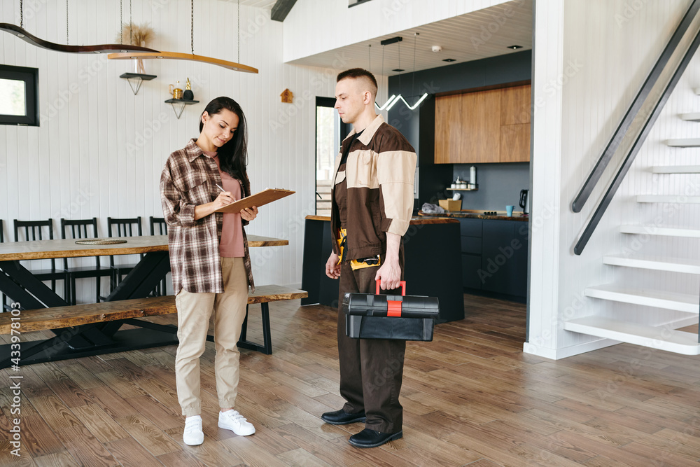 Young woman signing paper after receiving plumbing service while standing in front of plumber Young woman signing paper after receiving plumbing service while standing in front of plumber