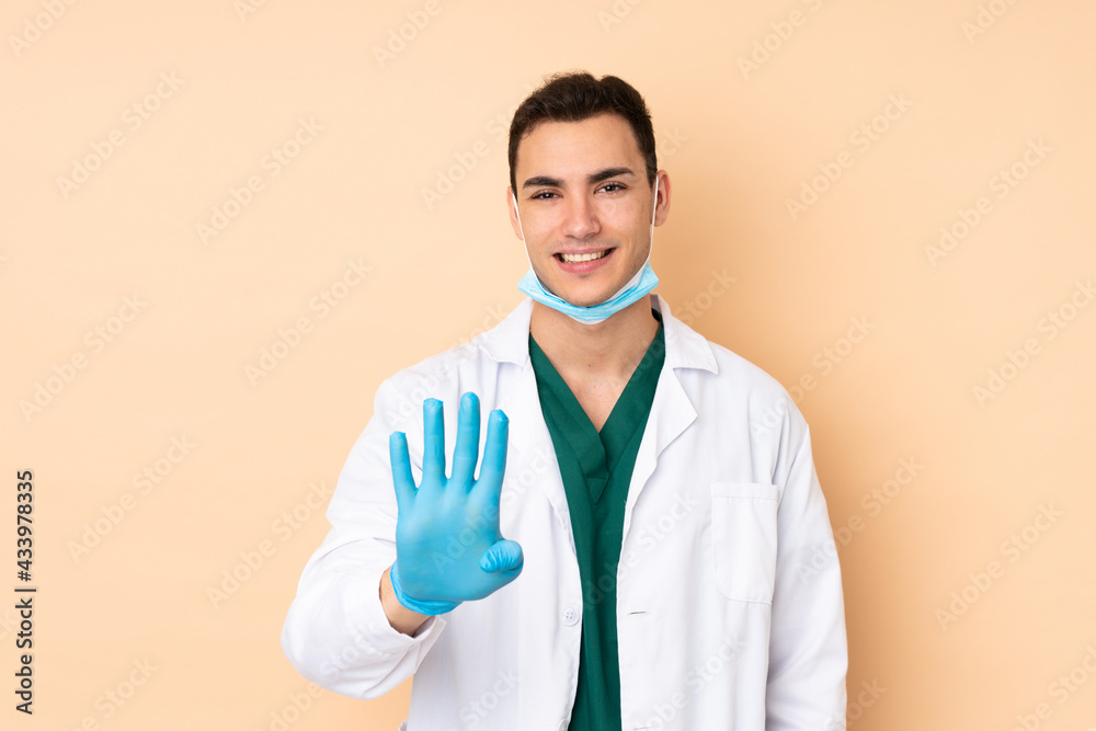 Young dentist man holding tools isolated on beige background happy and counting four with fingers Young dentist man holding tools isolated on beige background happy and counting four with fingers