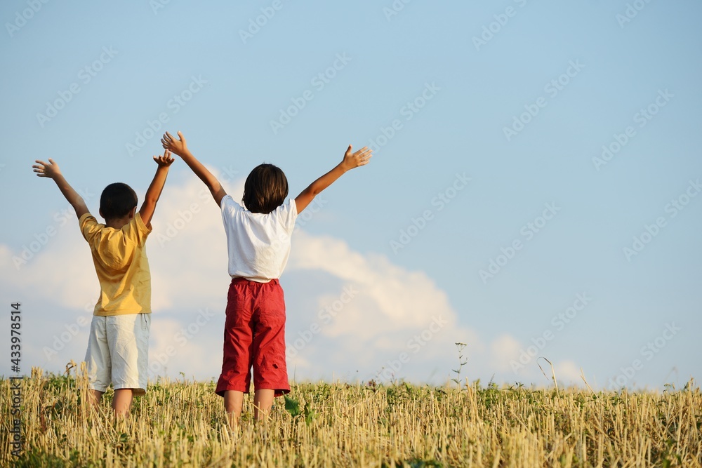 Two kids standing on meadow with arms up in air Two kids standing on meadow with arms up in air