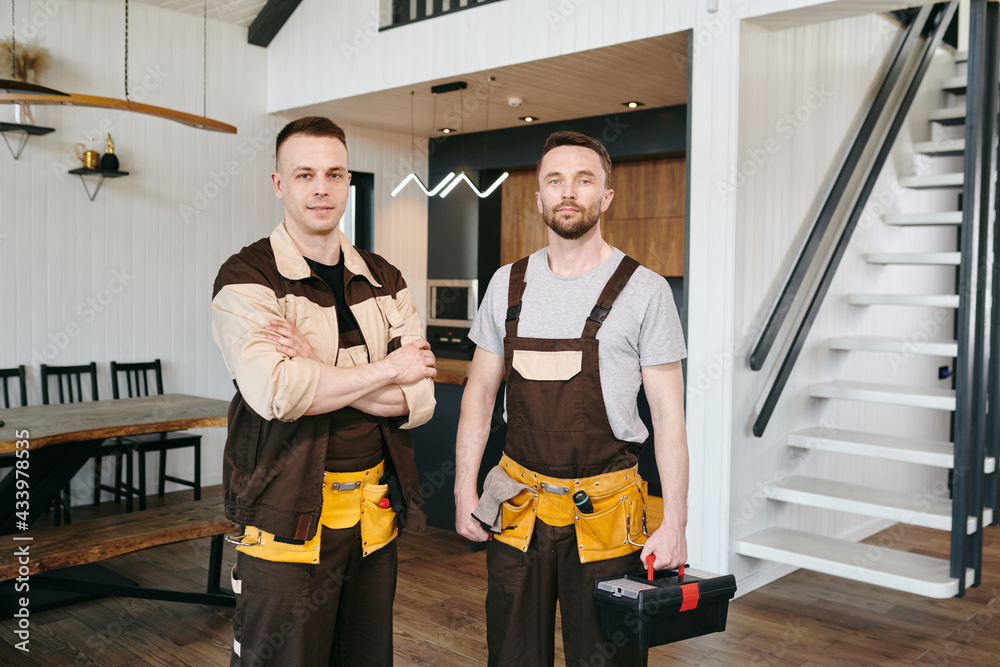 Obraz premium Two plumbers in uniform standing in front of camera in living-room of large house