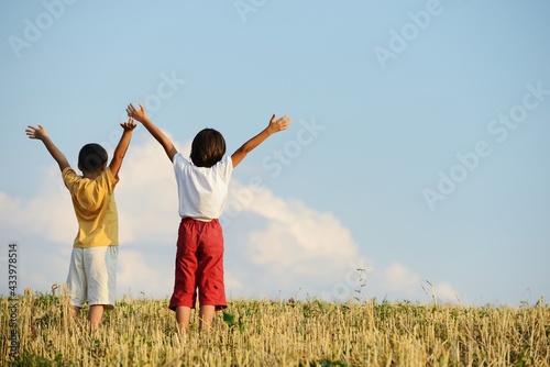 Two kids standing on meadow with arms up in air