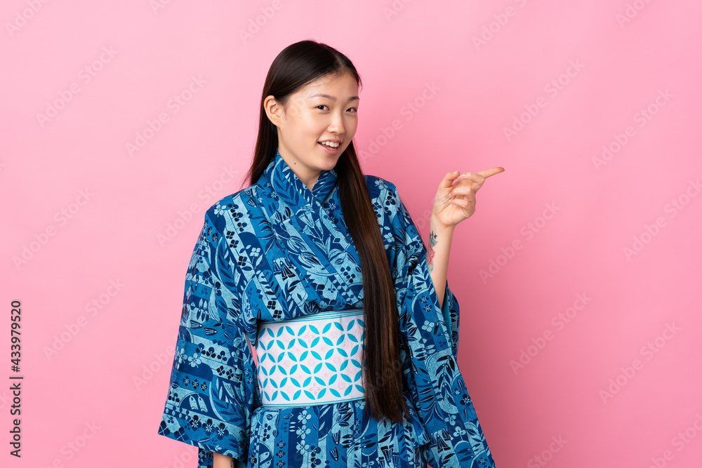 Young Chinese girl wearing kimono over isolated background pointing finger to the side and presenting a product Young Chinese girl wearing kimono over isolated background pointing finger to the side and presenting a product