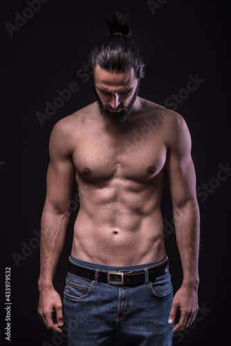 Studio portrait of a beautiful masculine bearded shirtless man. Low Key photo of male athletic body.