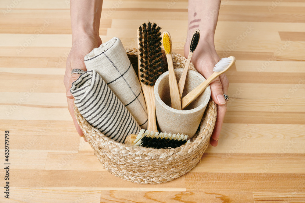 A hand holding a basket of wooden brushes and folded towels over table